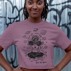Black woman  wearing a pink ROCKaBLOCK cropped t-shirt with a graphic yoga inspired "Give me space" design in front of a graffiti-covered wall.