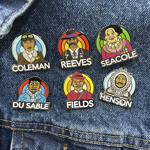 A collection of ROCKaBLOCK hard enamel Pioneers pins with characters including Bessie Coleman, Bass Reeves, 'Stagecoach' Mary Fields, Jean Baptiste Point Du Sable, Mary Seacole, and Matthew Henson, secured on a denim fabric. Highlighting Black history.