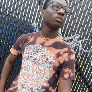 Person wearing a tie-dye t-shirt with text in front of a chain-link fence.