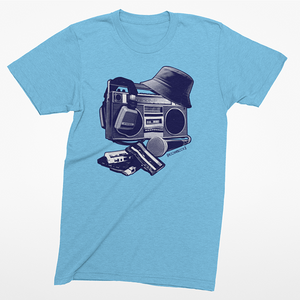 A light blue heather crewneck t-shirt featuring a graphic print of a retro boombox with a hat, headphones, and a cassette deck on the front, displayed against a clean white background.