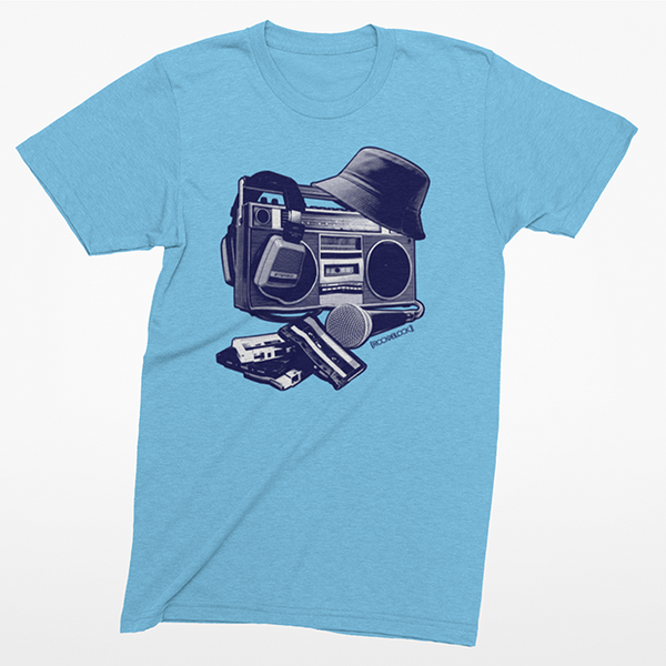 A light blue heather crewneck t-shirt featuring a graphic print of a retro boombox with a hat, headphones, and a cassette deck on the front, displayed against a clean white background.