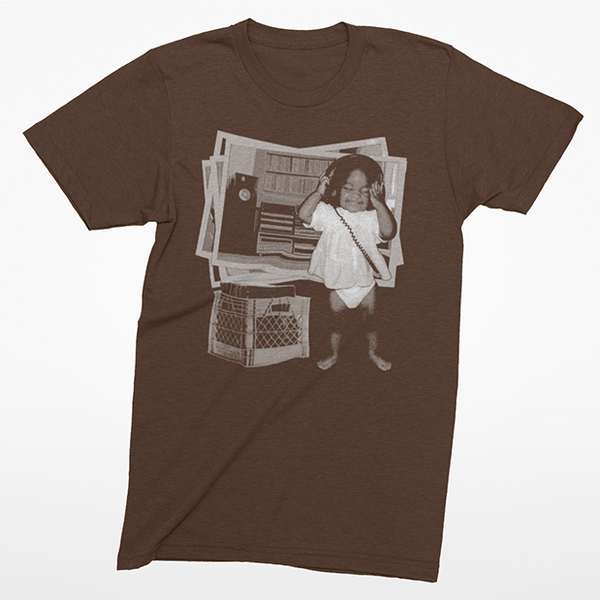 A brown short-sleeve crewneck t-shirt featuring a vintage-style graphic print of a young girl in a white dress standing in front of a speaker and crates.